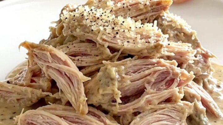 A mound of tender shredded Caesar chicken topped with parmesan cheese in a slow cooker.
