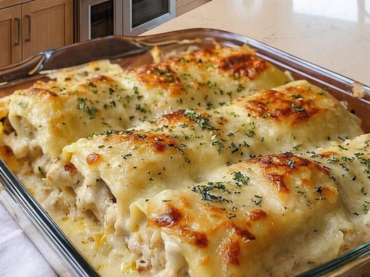 A close-up of a chicken Alfredo lasagna roll with a visible cheese pull on a wooden board.