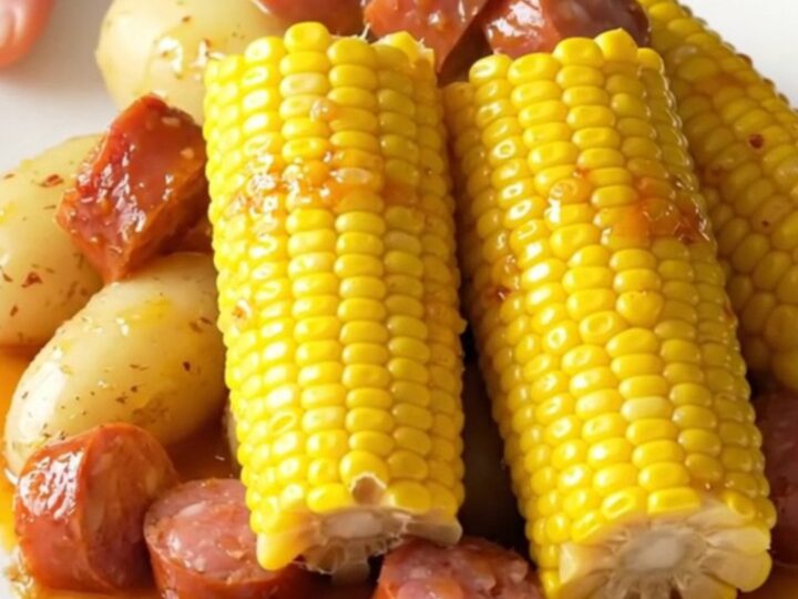 A high-angle view of a slow cooker filled with chunks of smoked sausage, baby potatoes