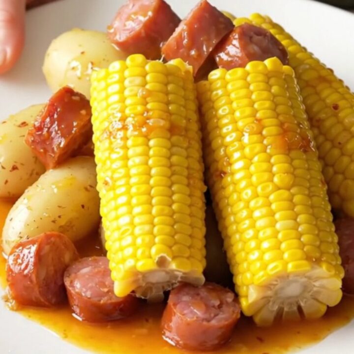 A high-angle view of a slow cooker filled with chunks of smoked sausage, baby potatoes