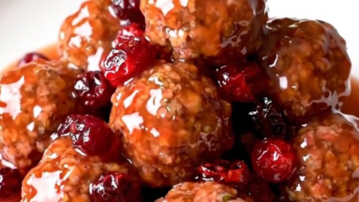 A slow cooker filled with turkey meatballs coated in a glossy, dark red cranberry orange sauce.