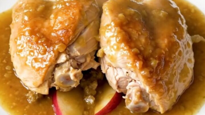 A plate of slow-cooked chicken thighs with soft apples and onions in a rich Dijon sauce.
