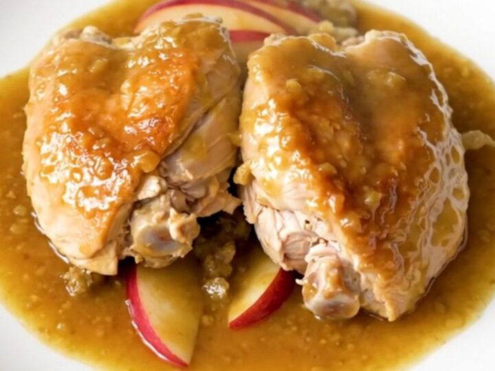 A plate of slow-cooked chicken thighs with soft apples and onions in a rich Dijon sauce.
