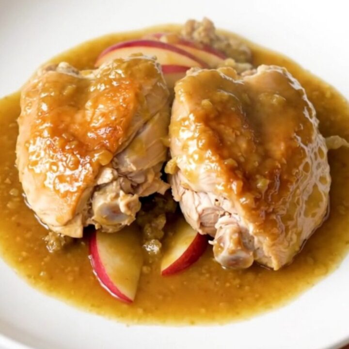 A plate of slow-cooked chicken thighs with soft apples and onions in a rich Dijon sauce.
