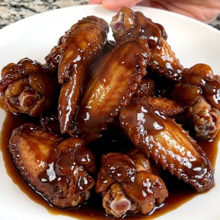 A close-up of dark, glazed chicken wings on a white plate with a glossy, thick soy molasses sauce and light steam.