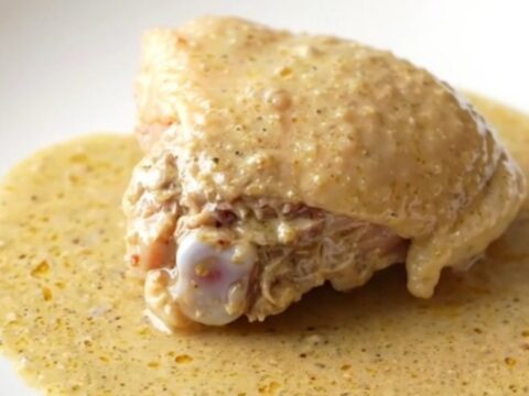 A close-up of a bone-in chicken thigh covered in thick, creamy gravy inside a slow cooker pot.