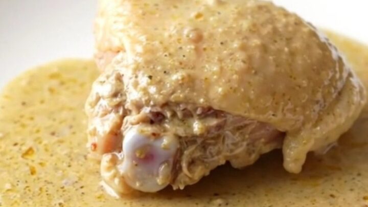 A close-up of a bone-in chicken thigh covered in thick, creamy gravy inside a slow cooker pot.