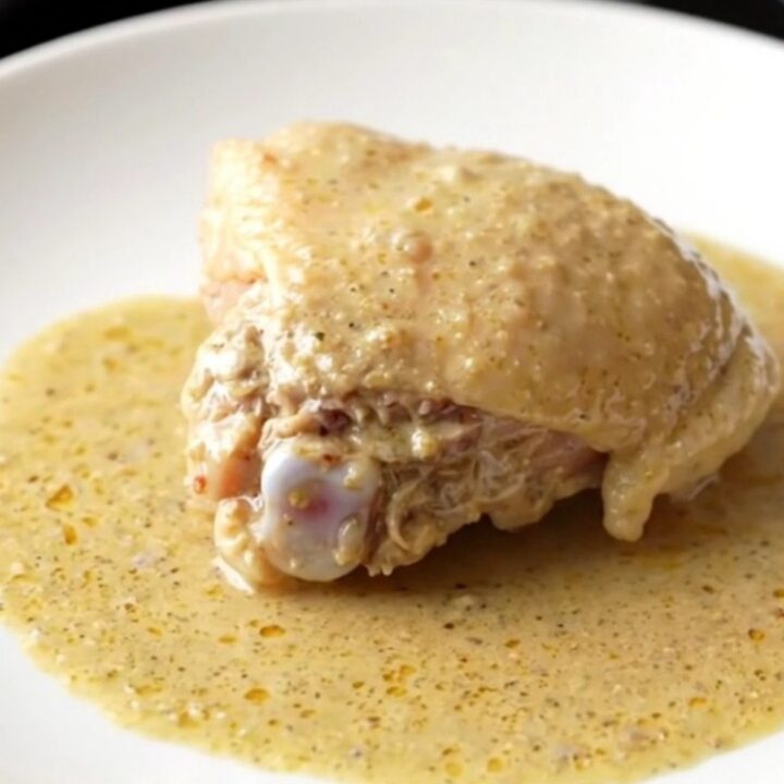 A close-up of a bone-in chicken thigh covered in thick, creamy gravy inside a slow cooker pot.