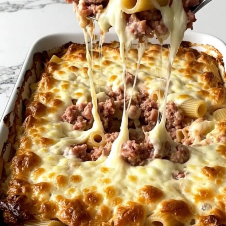 A top-down view of a rectangular baking dish filled with raw rigatoni, sausage crumbles, and creamy vodka sauce.