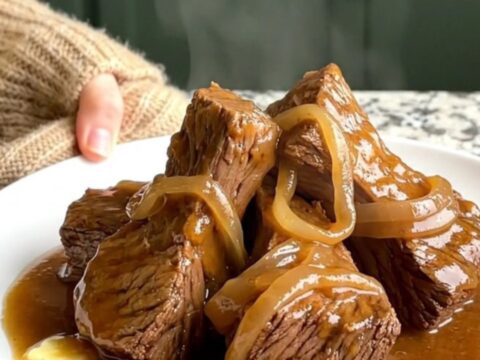 A close-up shot of slow-cooked beef tips in a rich onion gravy served on a white plate.