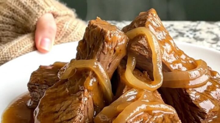 A close-up shot of slow-cooked beef tips in a rich onion gravy served on a white plate.