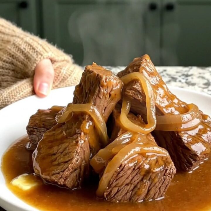 A close-up shot of slow-cooked beef tips in a rich onion gravy served on a white plate.