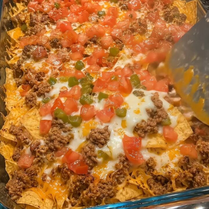 A glass baking dish filled with loaded beef nachos featuring melted cheese, ground beef, and fresh colorful toppings.