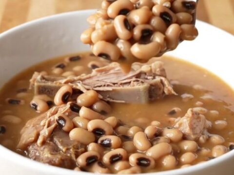 A stainless steel slow cooker filled with smoked turkey wings, black-eyed peas, and a rich tomato-based broth.