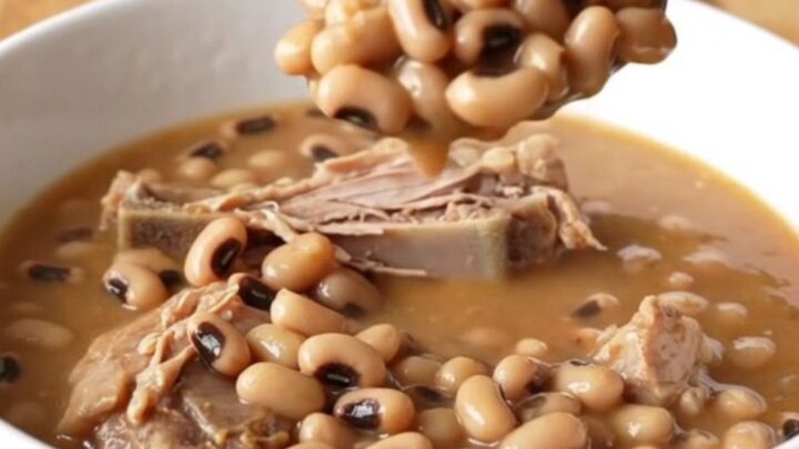 A stainless steel slow cooker filled with smoked turkey wings, black-eyed peas, and a rich tomato-based broth.