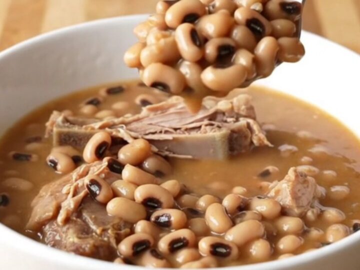 A stainless steel slow cooker filled with smoked turkey wings, black-eyed peas, and a rich tomato-based broth.