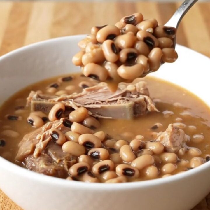 A stainless steel slow cooker filled with smoked turkey wings, black-eyed peas, and a rich tomato-based broth.