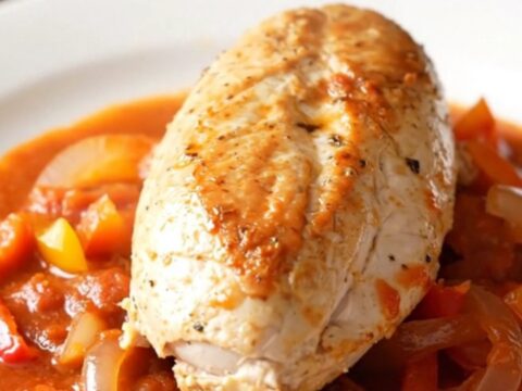 A close-up of tender chicken breast topped with colorful red and yellow peppers in a rich tomato sauce.
