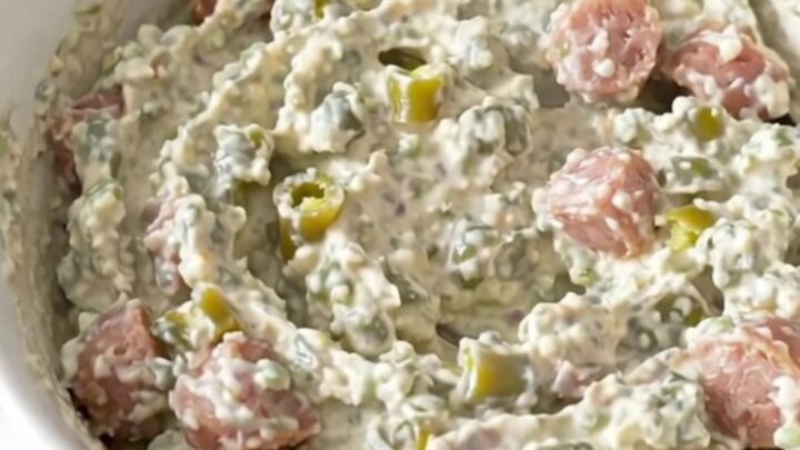 A creamy, sausage-filled green chile dip served in a white bowl with a warm, inviting steam rising from the surface.