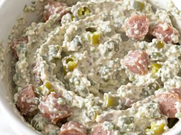 A creamy, sausage-filled green chile dip served in a white bowl with a warm, inviting steam rising from the surface.
