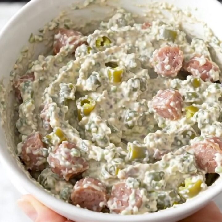 A creamy, sausage-filled green chile dip served in a white bowl with a warm, inviting steam rising from the surface.