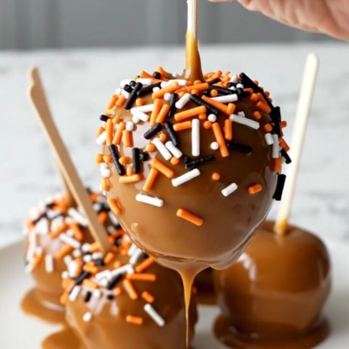 A group of crisp red apples on sticks, coated in thick caramel and festive orange and black sprinkles.