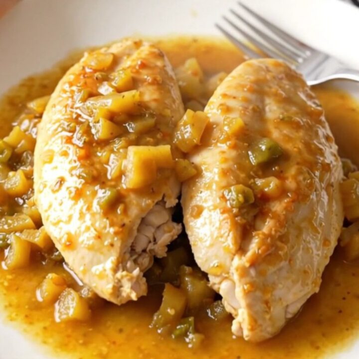 A close-up of tender, braised chicken breasts topped with a colorful mixture of giardiniera vegetables.