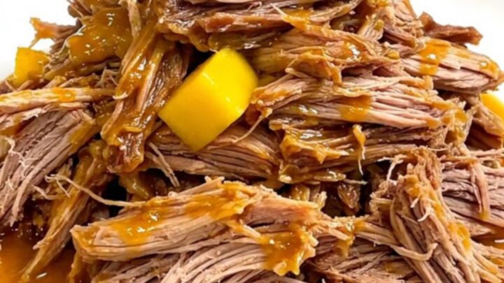 A close-up of tender mango habanero pulled pork served on a white plate with visible strands of meat and soft mango pieces.