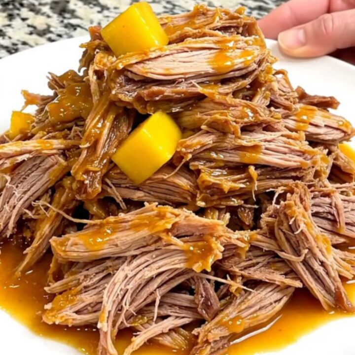 A close-up of tender mango habanero pulled pork served on a white plate with visible strands of meat and soft mango pieces.