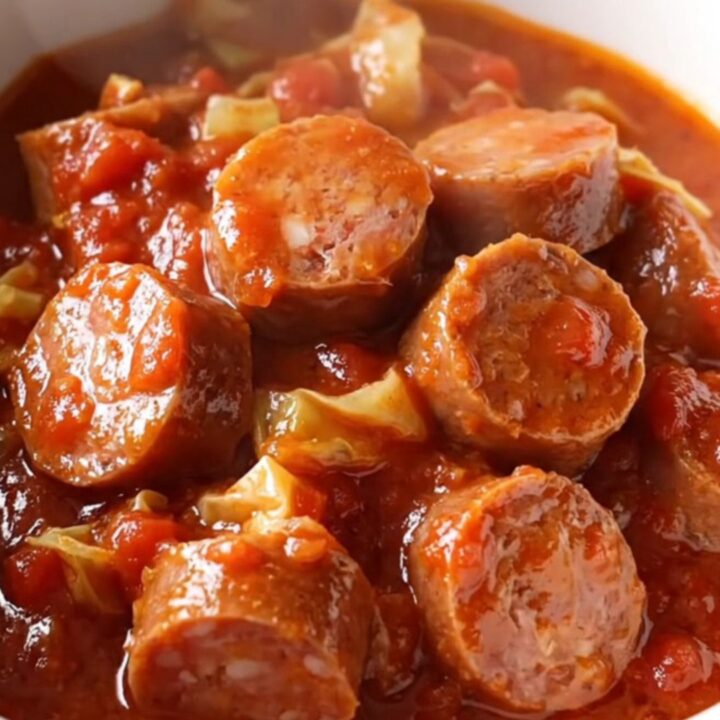 A close-up of a slow cooker filled with Italian sausage coins, cabbage, and rich tomato sauce.