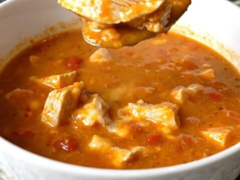 A white shallow bowl filled with creamy chicken parmesan soup, showcasing tender chicken pieces and melted cheese in a rich