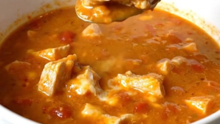 A white shallow bowl filled with creamy chicken parmesan soup, showcasing tender chicken pieces and melted cheese in a rich