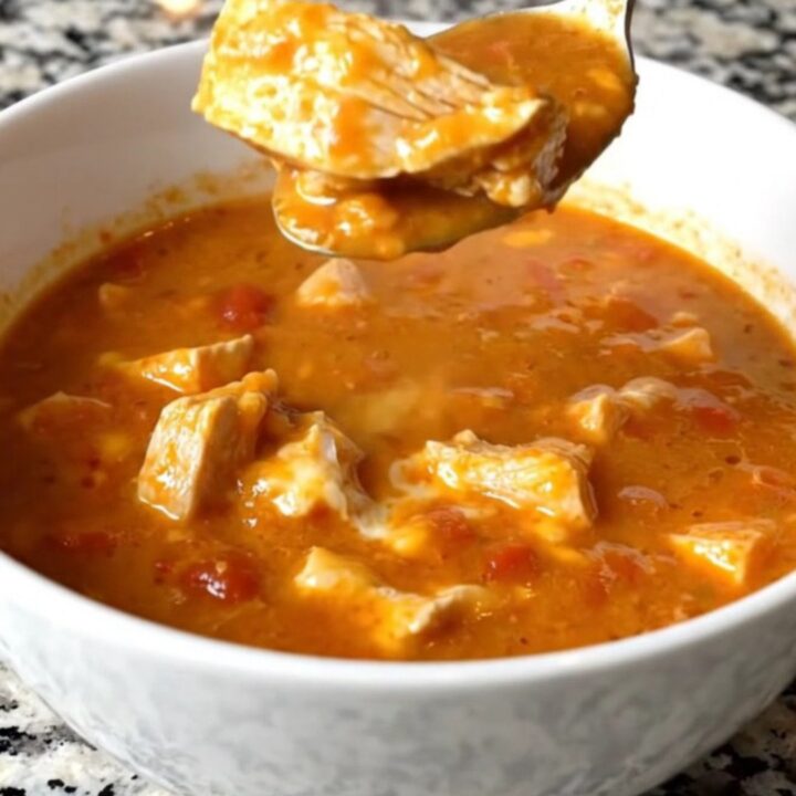 A white shallow bowl filled with creamy chicken parmesan soup, showcasing tender chicken pieces and melted cheese in a rich