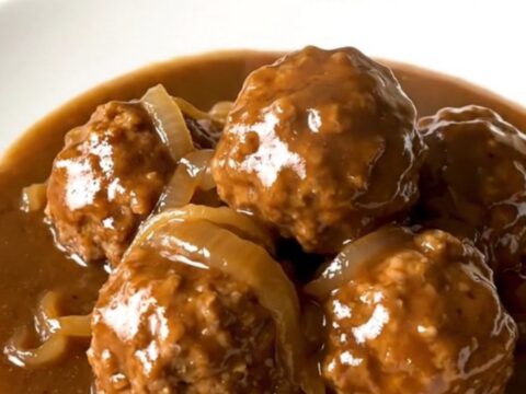 A slow cooker filled with beef meatballs in a rich brown onion gravy.
