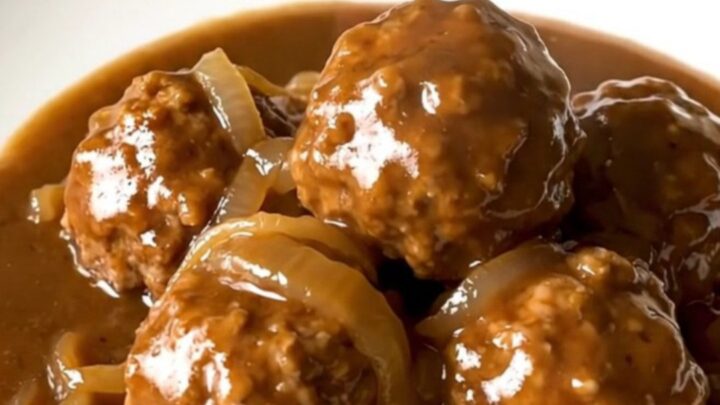 A slow cooker filled with beef meatballs in a rich brown onion gravy.