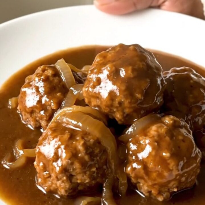A slow cooker filled with beef meatballs in a rich brown onion gravy.