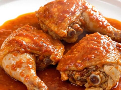 A close-up of slow-cooked chicken thighs in a rich tomato sauce with potatoes and olives in a slow cooker.