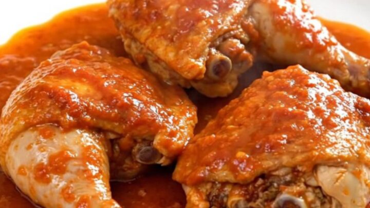 A close-up of slow-cooked chicken thighs in a rich tomato sauce with potatoes and olives in a slow cooker.