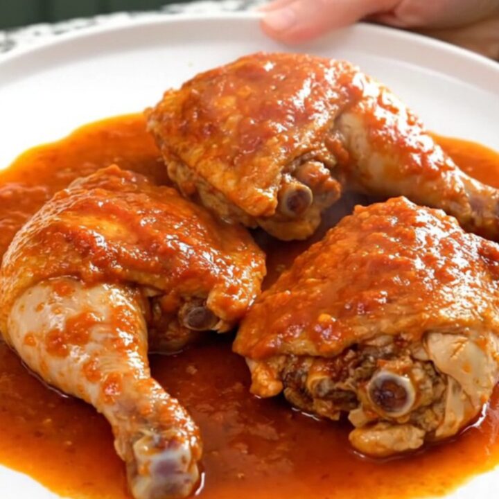 A close-up of slow-cooked chicken thighs in a rich tomato sauce with potatoes and olives in a slow cooker.