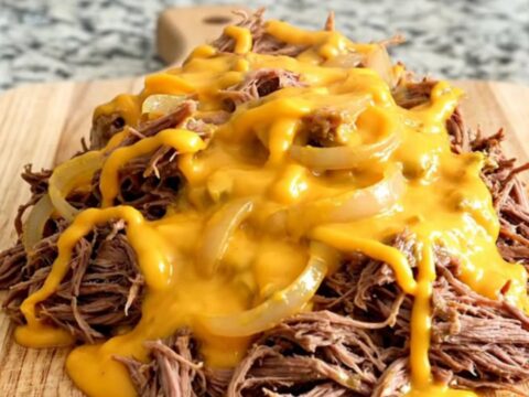 A pile of slow-cooked shredded beef sliders covered in creamy cheddar sauce on a rustic wooden board.