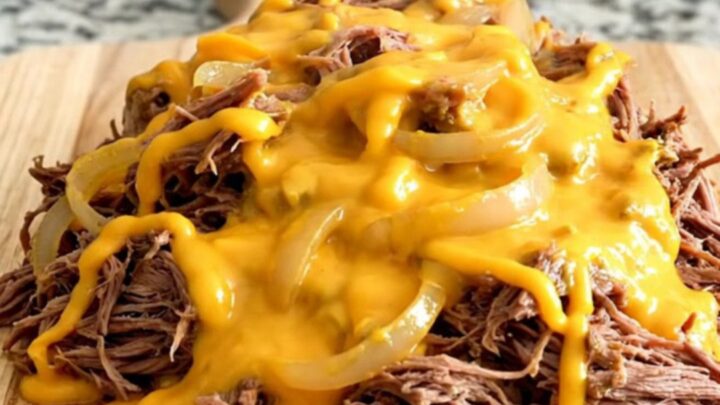 A pile of slow-cooked shredded beef sliders covered in creamy cheddar sauce on a rustic wooden board.
