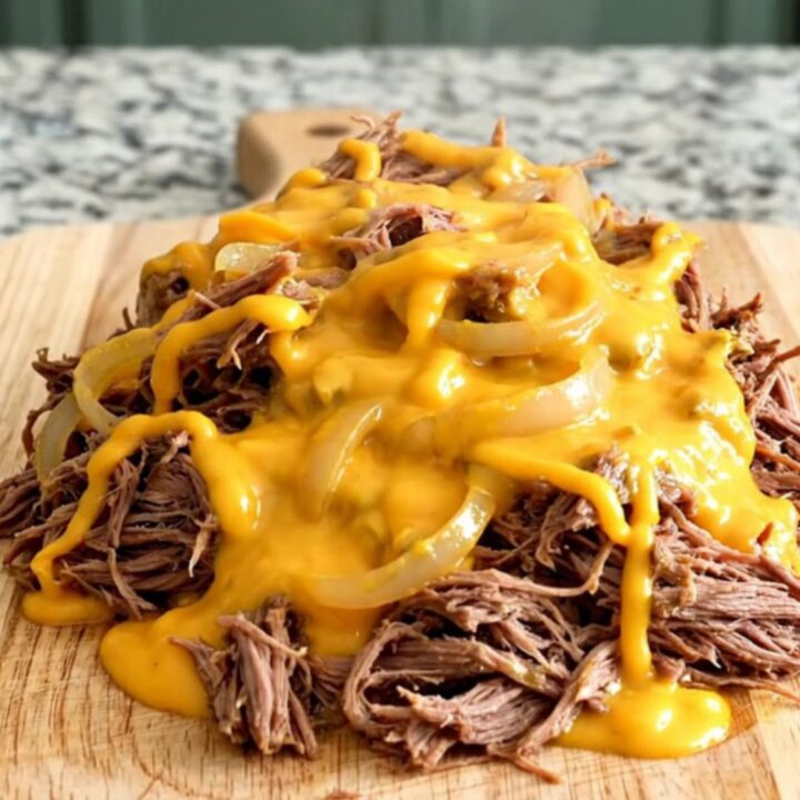 A pile of slow-cooked shredded beef sliders covered in creamy cheddar sauce on a rustic wooden board.