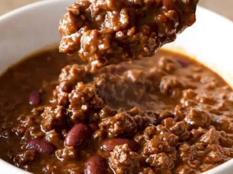 A close-up of a bowl filled with rich, dark brown beef and bean chili, garnished with a sprinkle of fresh herbs.