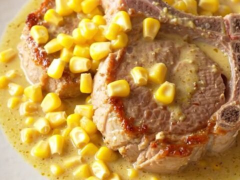 A close-up of tender, slow-cooked pork chops covered in a rich, creamy yellow corn sauce on a white plate.