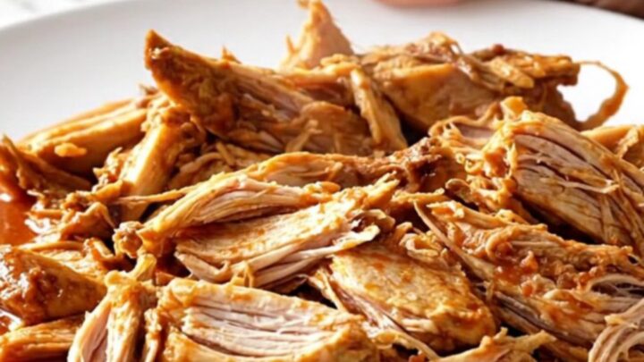 A close-up of tender shredded chicken Ropa Vieja in a rich tomato sauce with peppers and olives.