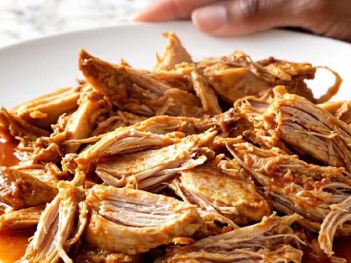 A close-up of tender shredded chicken Ropa Vieja in a rich tomato sauce with peppers and olives.