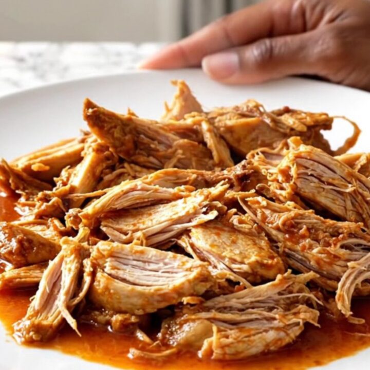 A close-up of tender shredded chicken Ropa Vieja in a rich tomato sauce with peppers and olives.
