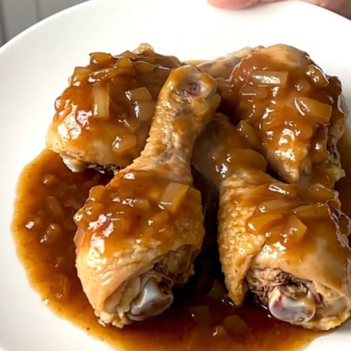 A plate of tender, slow-cooked chicken drumsticks coated in a glossy maple barbecue sauce with onions.