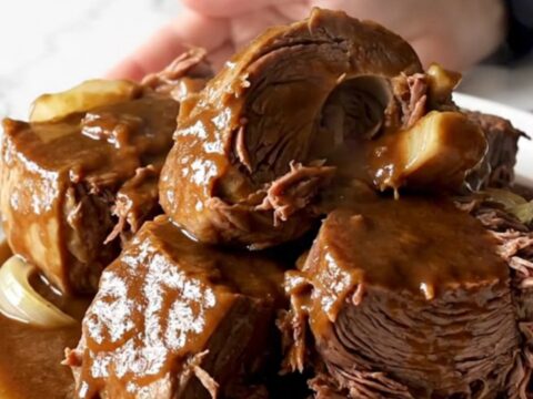 A close-up of a slow cooker filled with a tender beef chuck roast covered in a rich