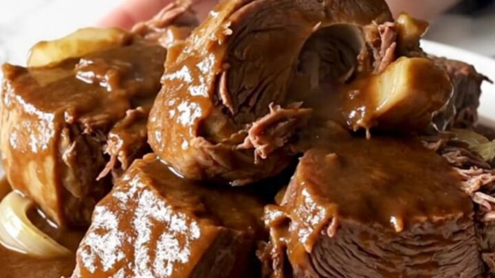 A close-up of a slow cooker filled with a tender beef chuck roast covered in a rich